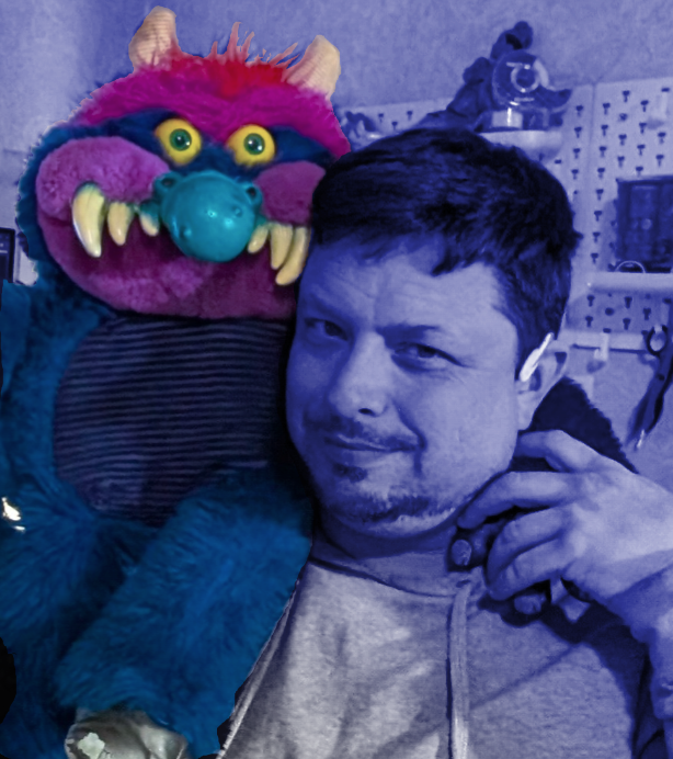 a middle aged white man with a shoddy beard in sa blue tinted photo where a my Pet Monster sits on his shoulder.